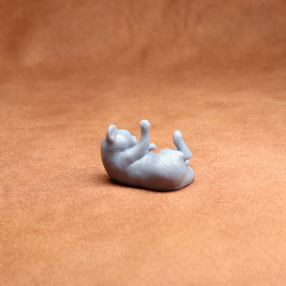 Small white figurine of a cat lying on its back on a brown surface