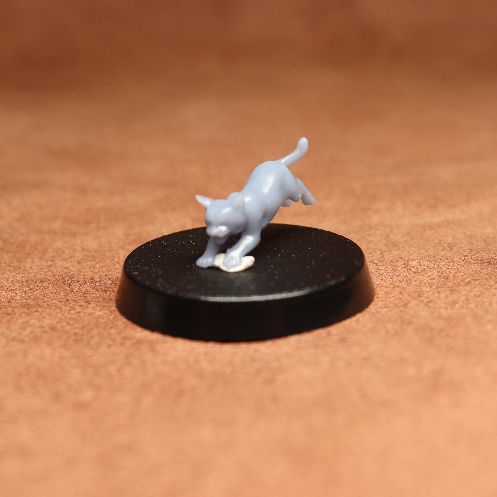 White figurine of a cat on a black round base against a brown background