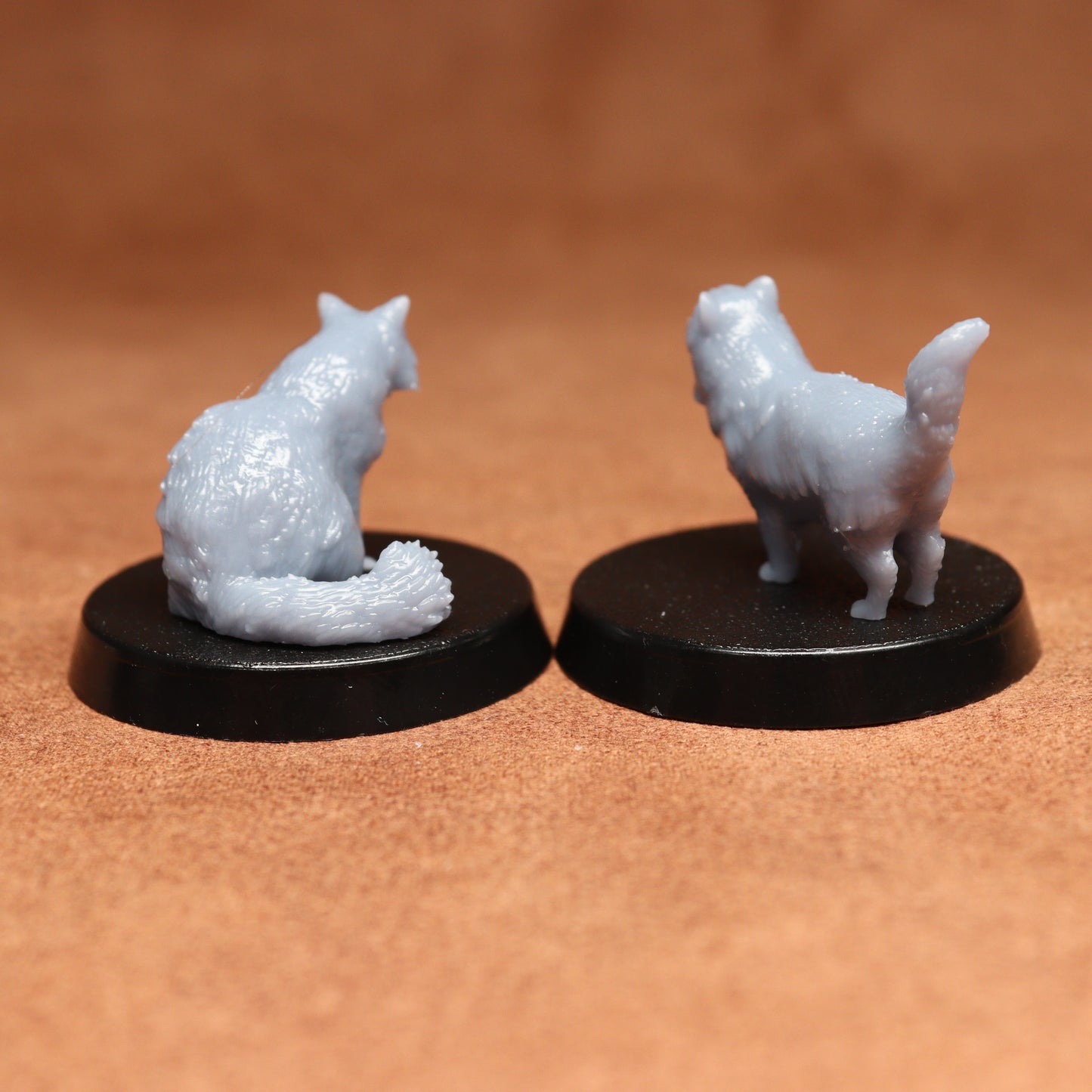 Two miniature cat figurines on black bases against a brown background
