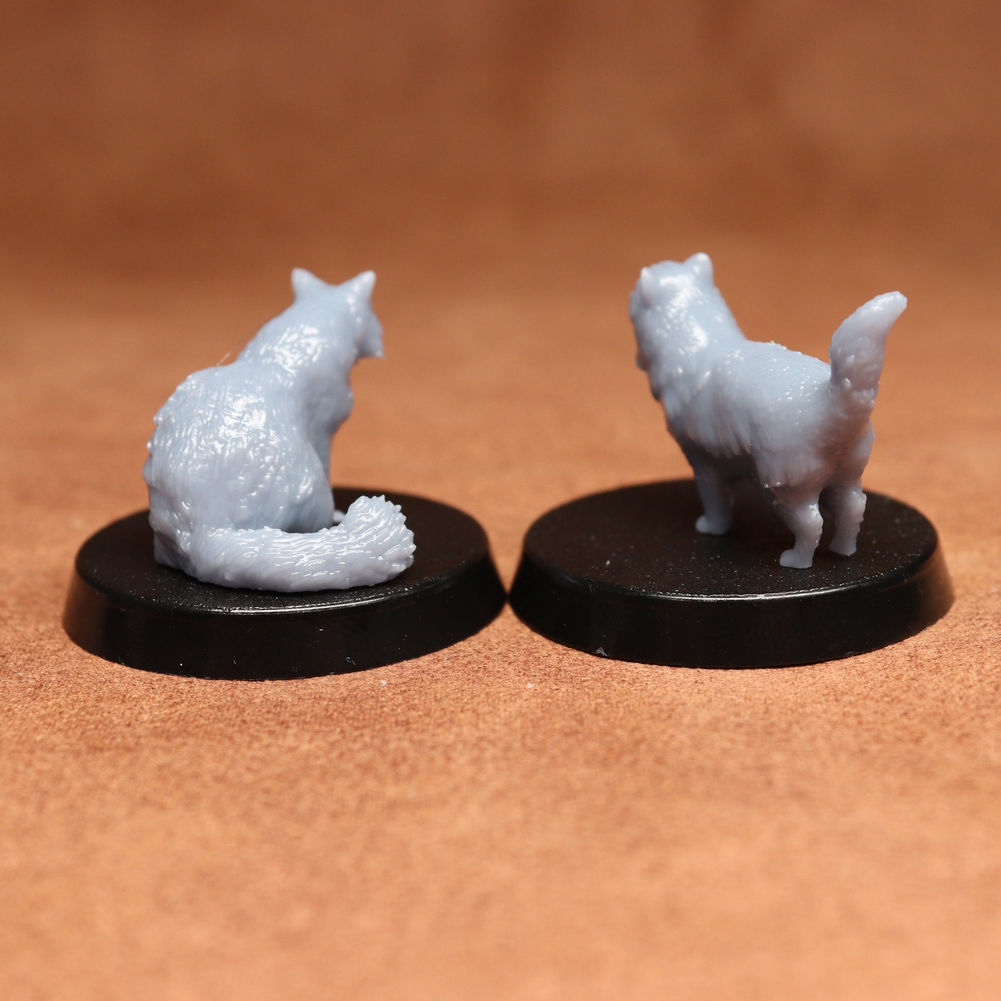 Two miniature cat figurines on black bases against a brown background