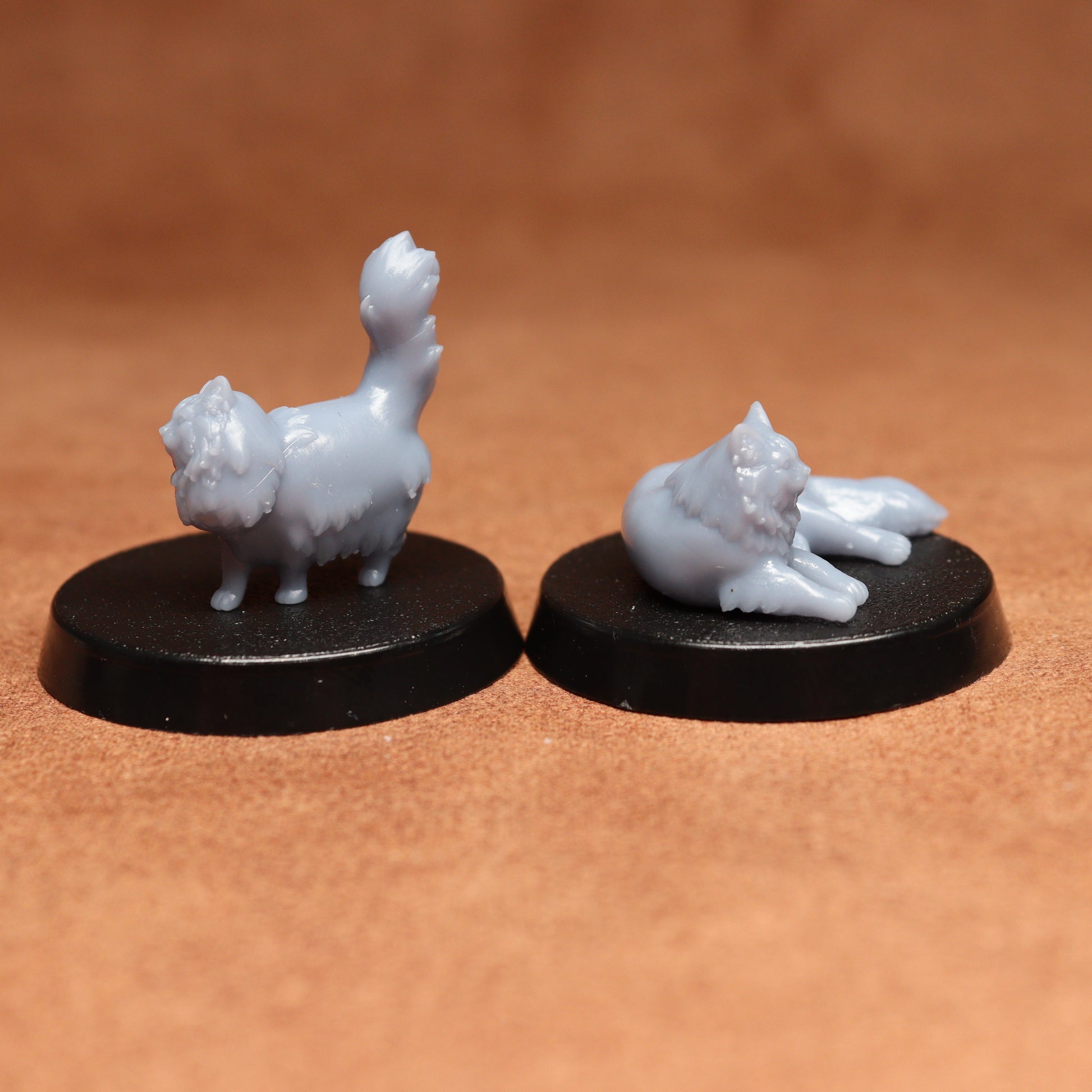 Two miniature cat figurines on black bases against a brown background