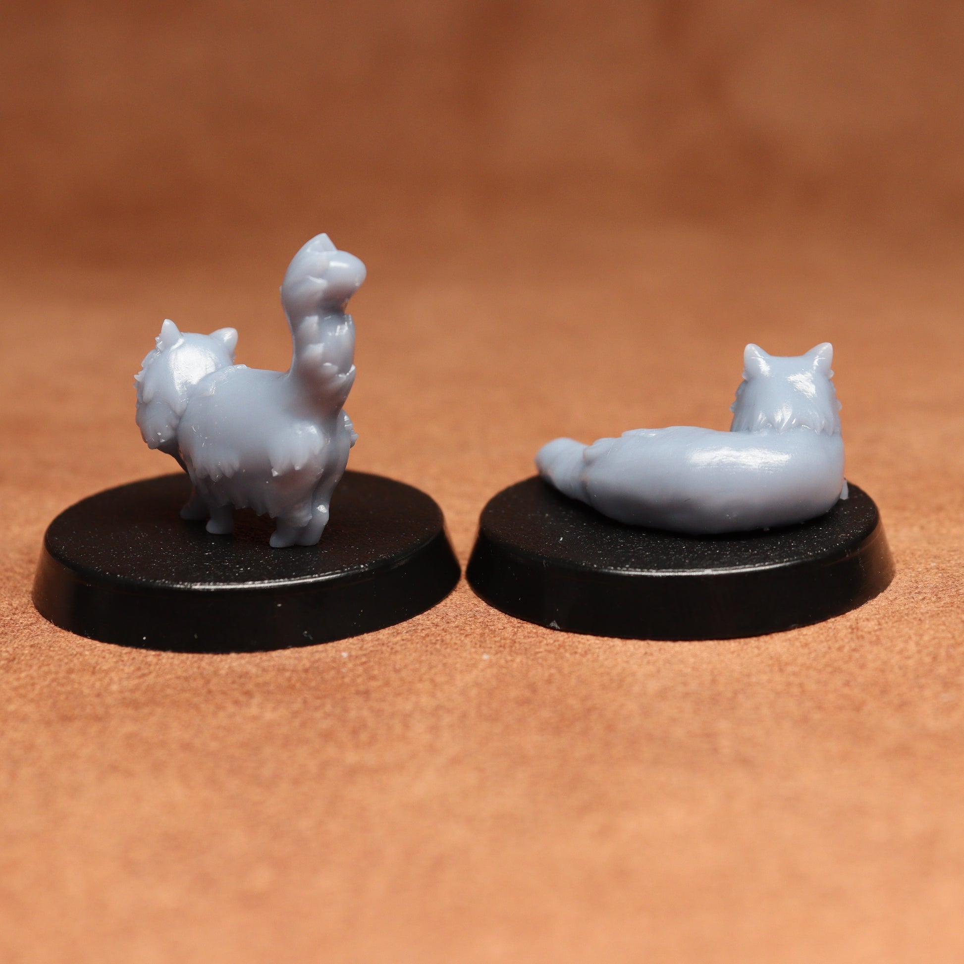 Two small gray cat figurines on black bases against a brown background
