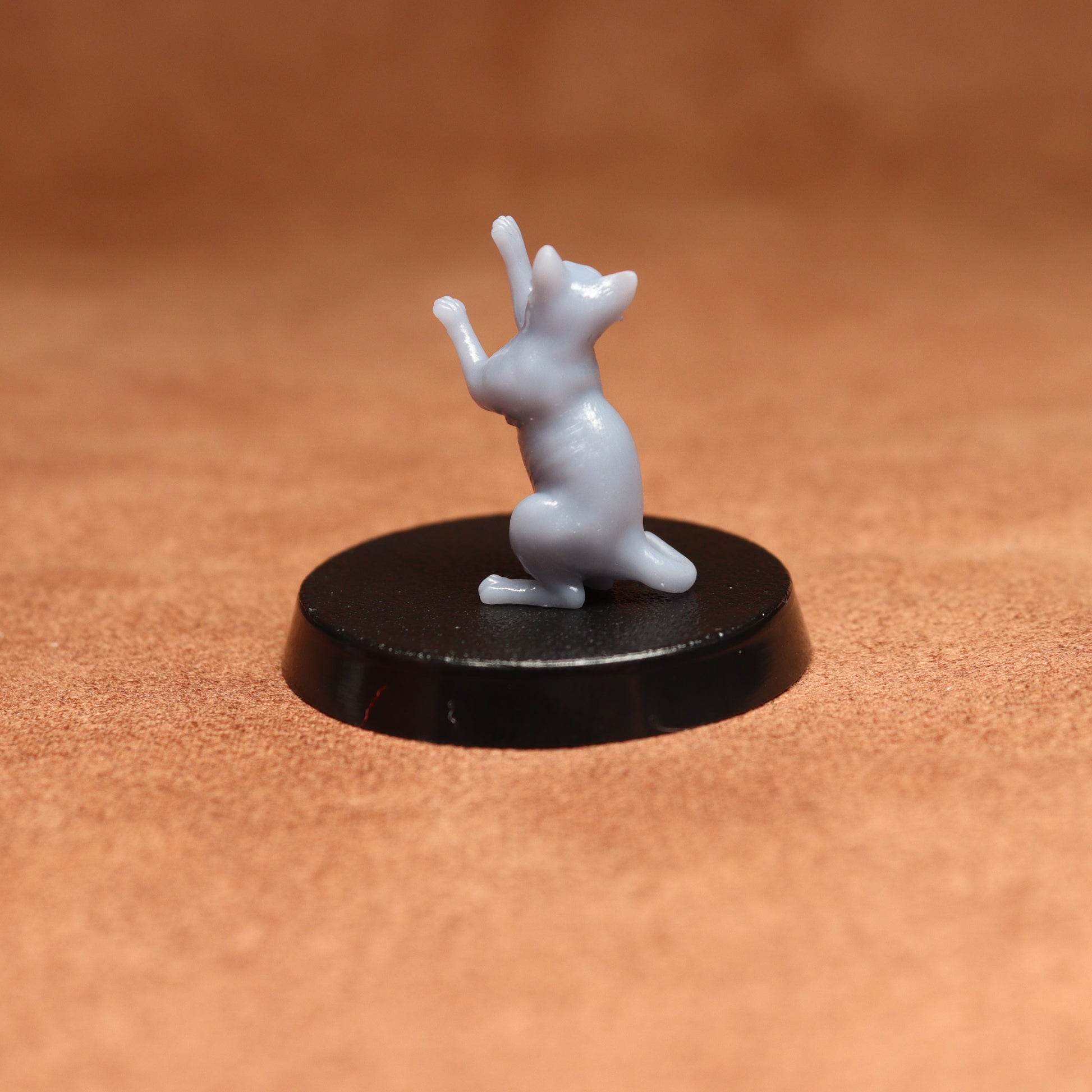 grey resin miniature cat figure on a black base with a brown background