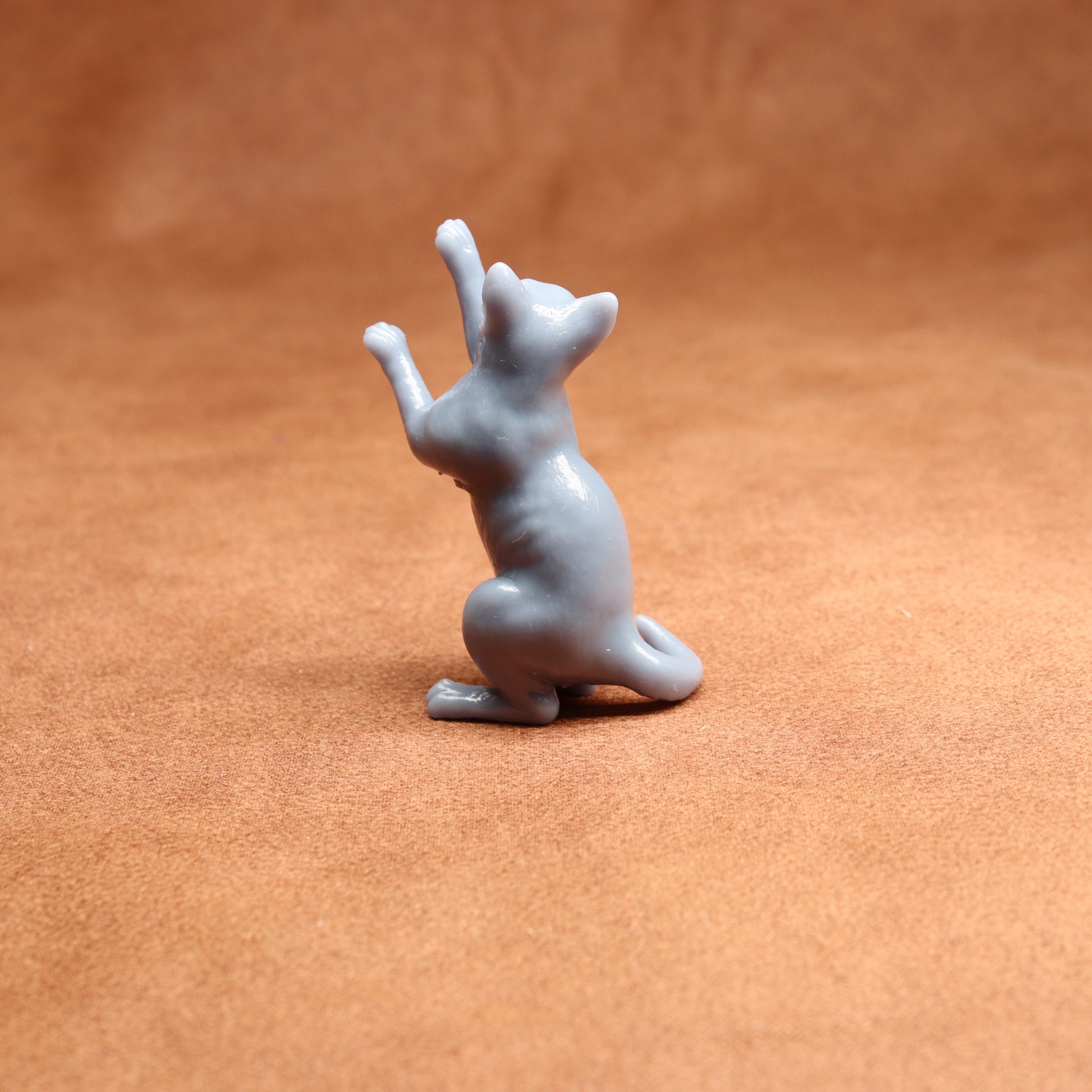 grey resin miniature cat figurine on a brown surface