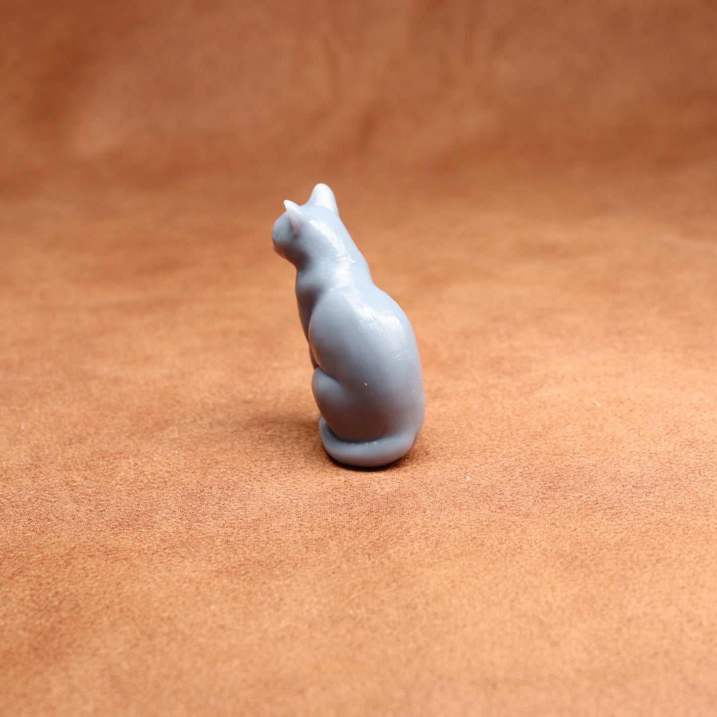 grey resin miniature cat figurine on a brown surface