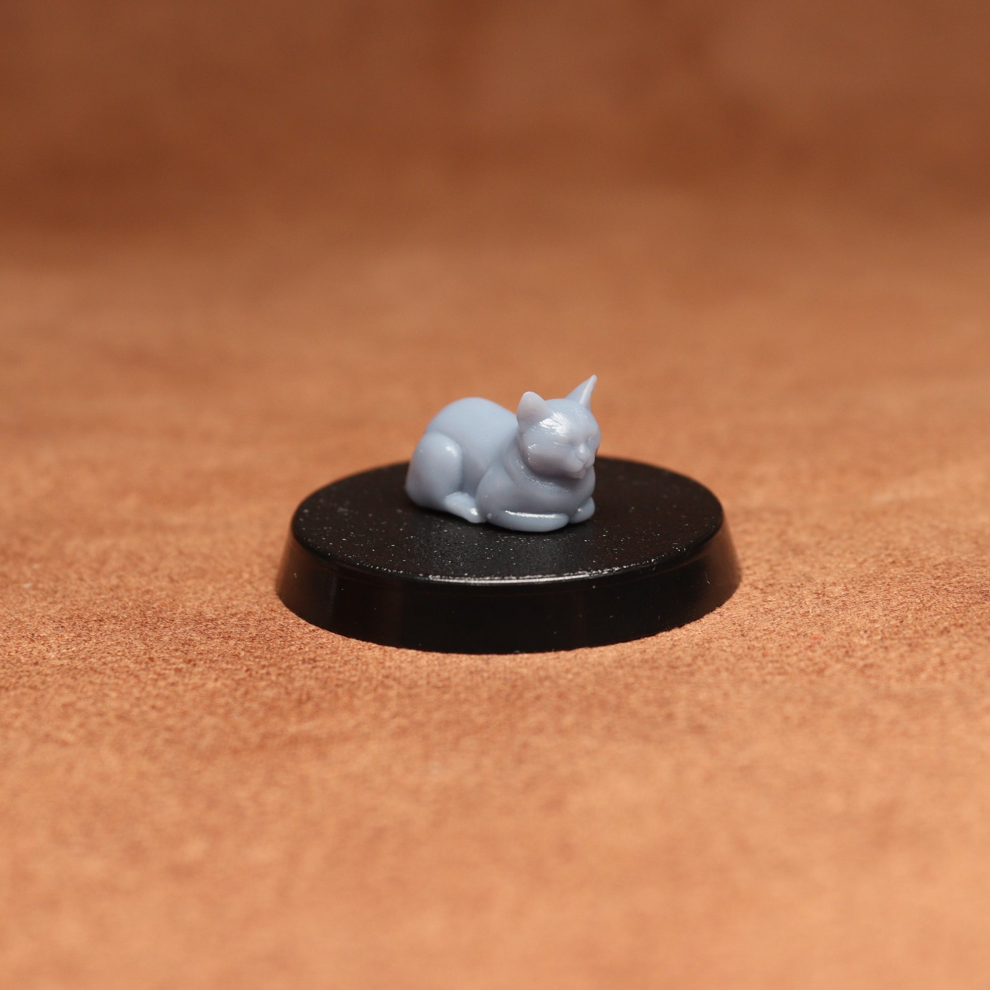 grey cat resin miniature on a black base on a brown background.