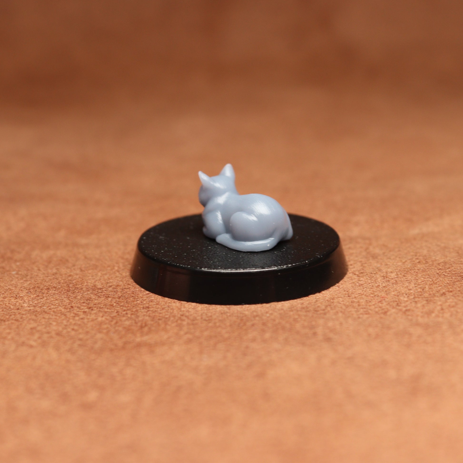 grey cat resin miniature on a black base on a brown background.
