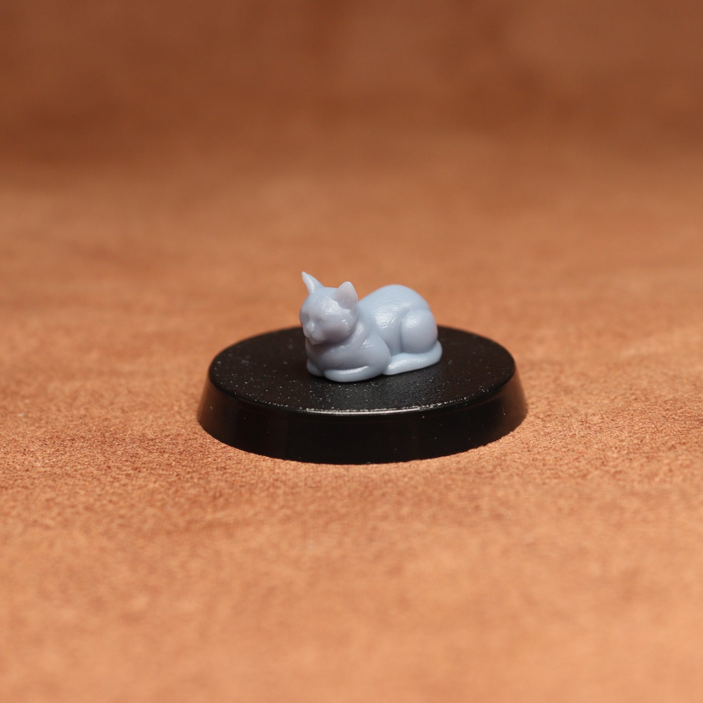 grey cat resin miniature on a black base on a brown background.
