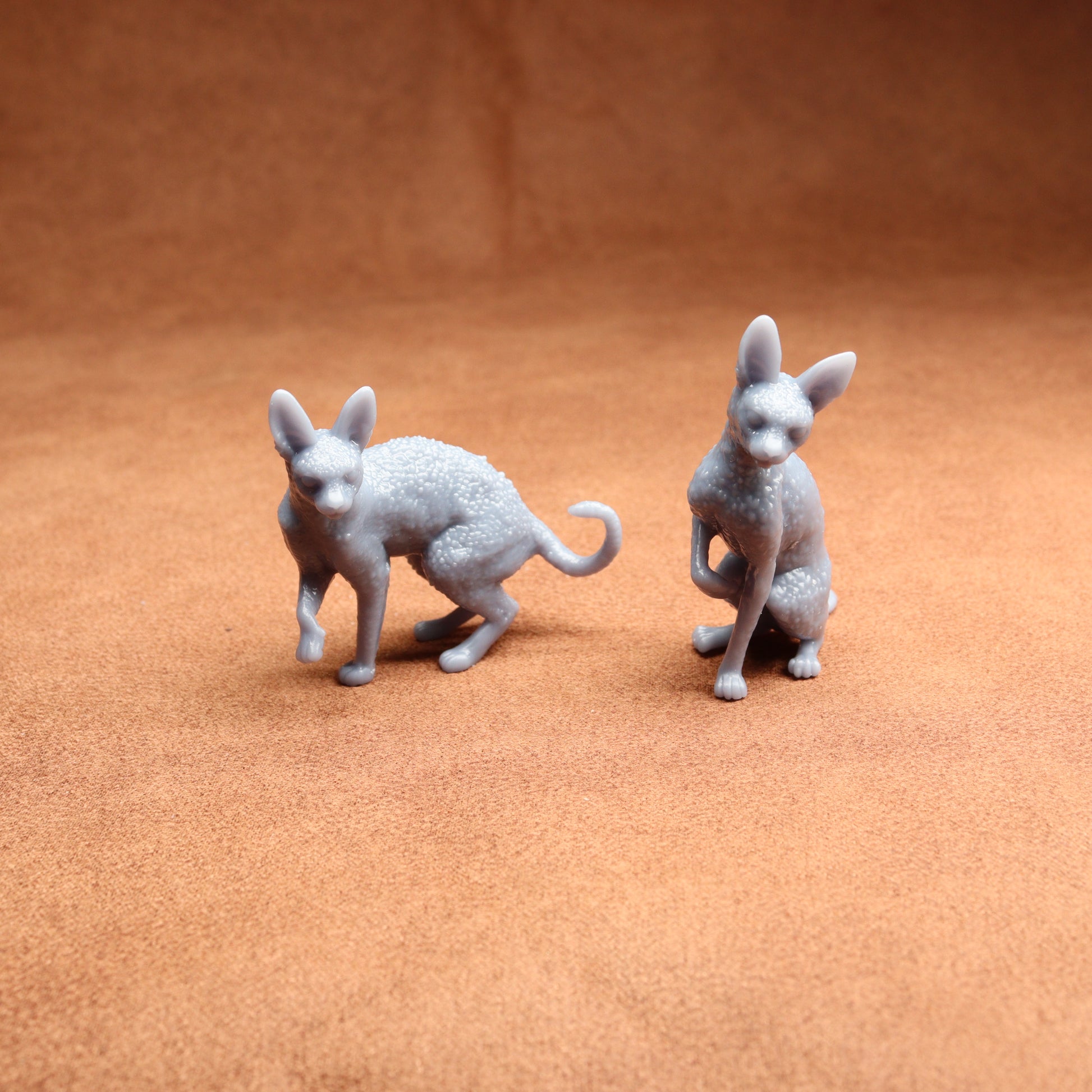 Two gray cat figurines on a brown surface