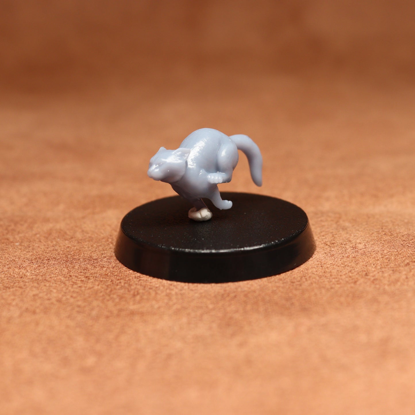 grey resin miniature cat figure on a black base with a brown background