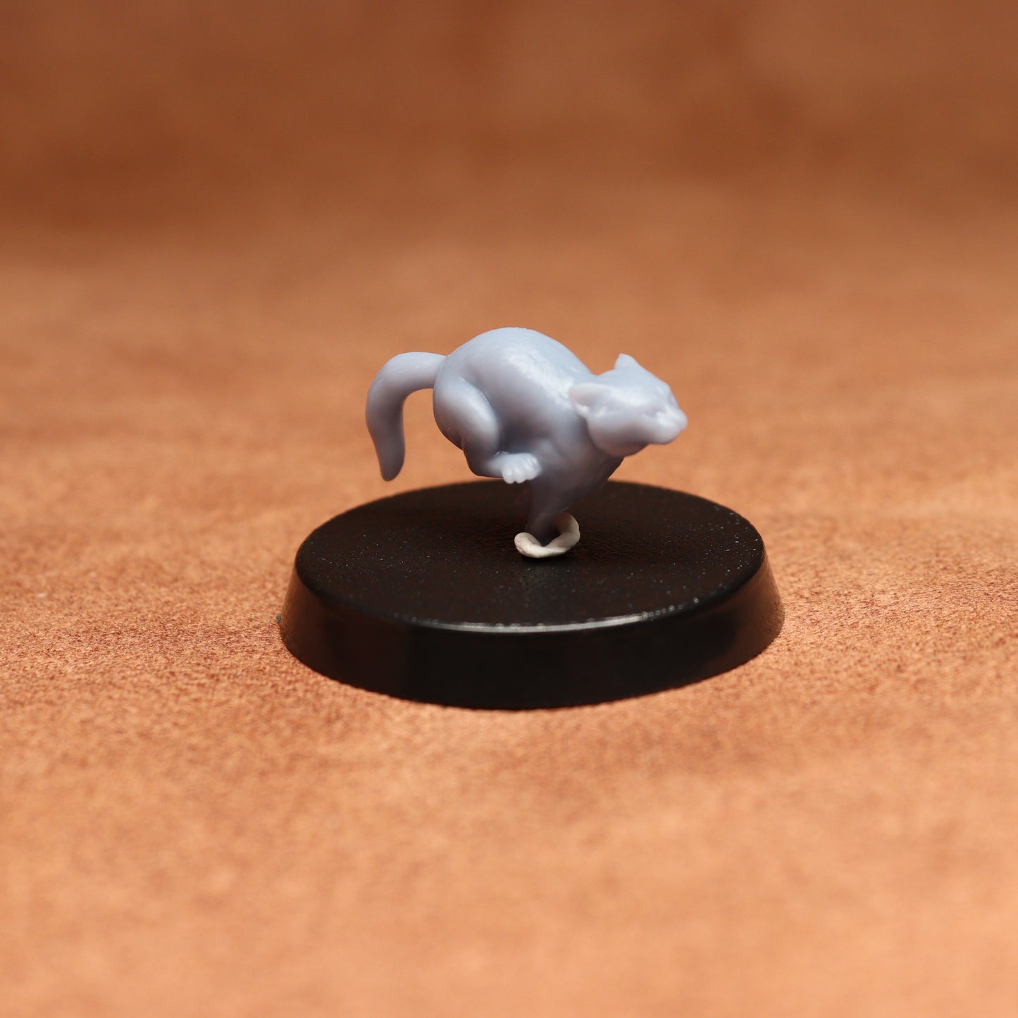 grey resin miniature cat figure on a black base with a brown background