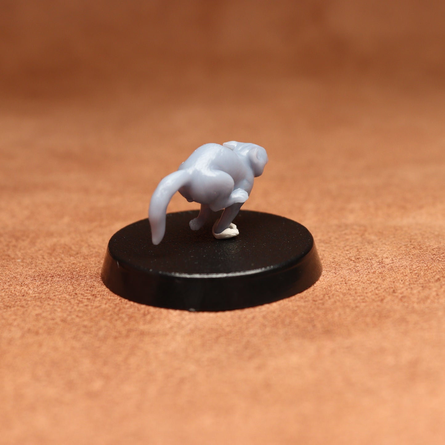 grey resin miniature cat figure on a black base with a brown background