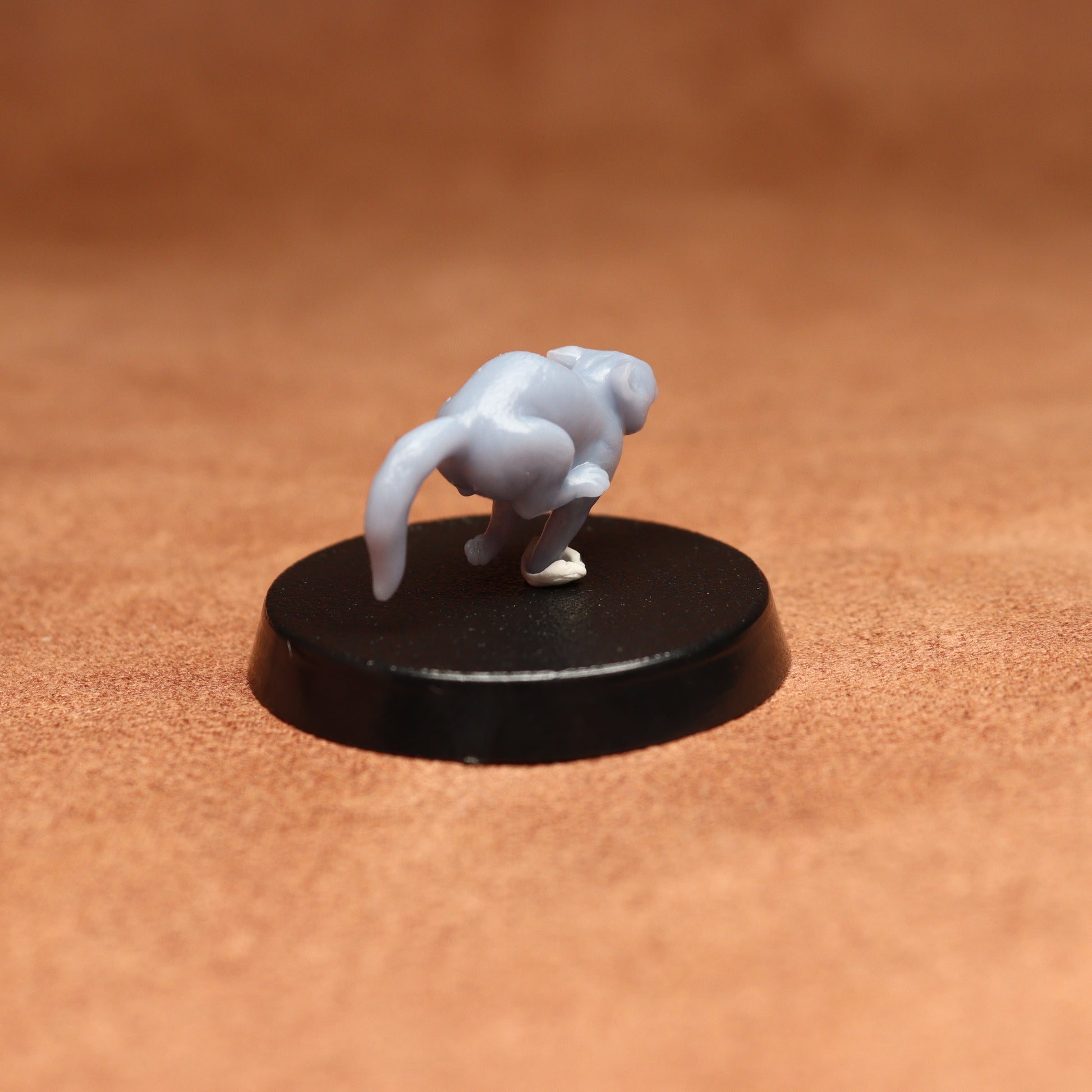 grey resin miniature cat figure on a black base with a brown background