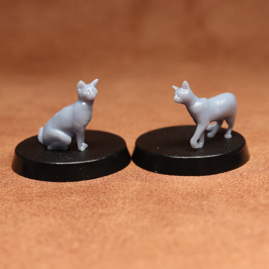Two small figurines of a cat and a cat on black bases against a brown background
