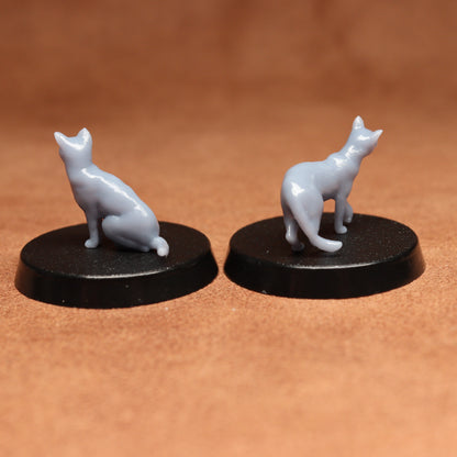 Two miniature cat figurines on black bases against a brown background