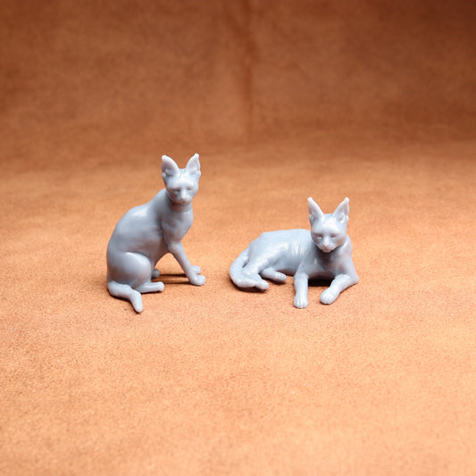 Two white cat figurines on a brown surface