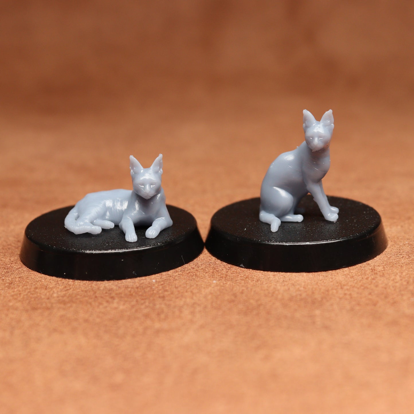 Two miniature cat figurines on black bases against a brown background