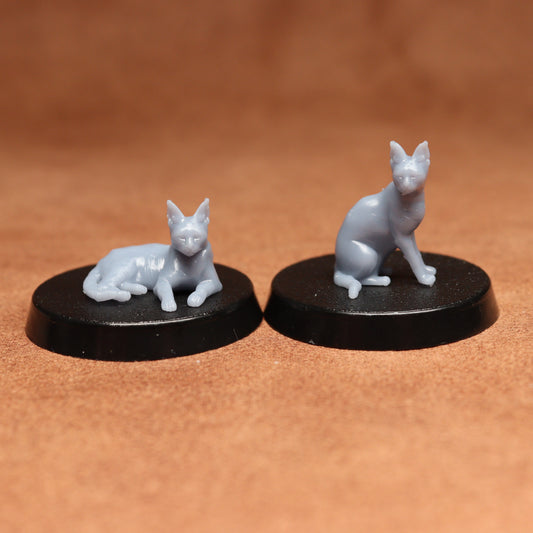 Two miniature cat figurines on black bases against a brown background