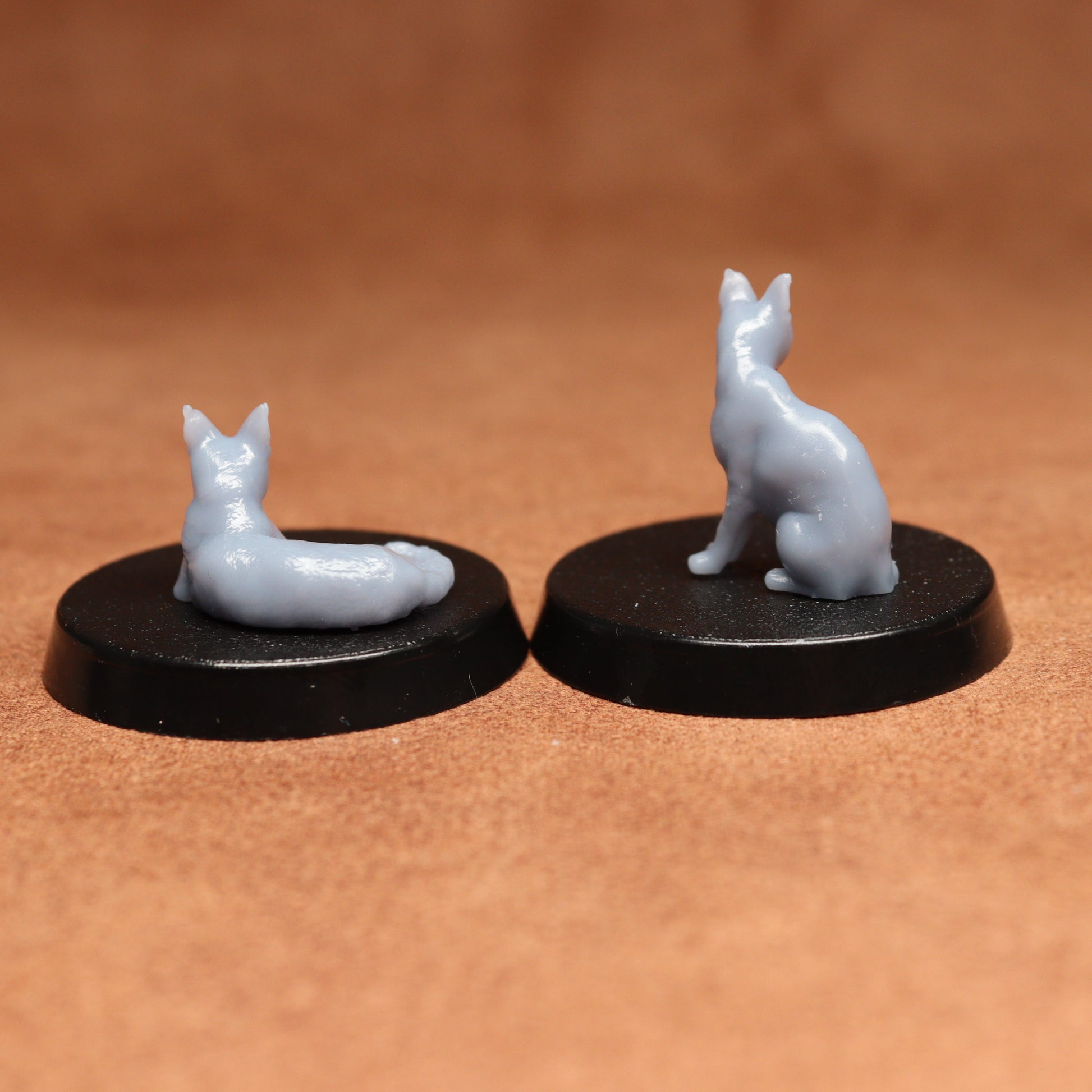 Two small gray cat figurines on black bases against a brown background