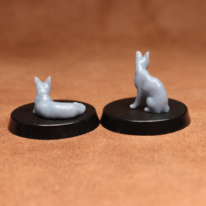 Two small gray cat figurines on black bases against a brown background