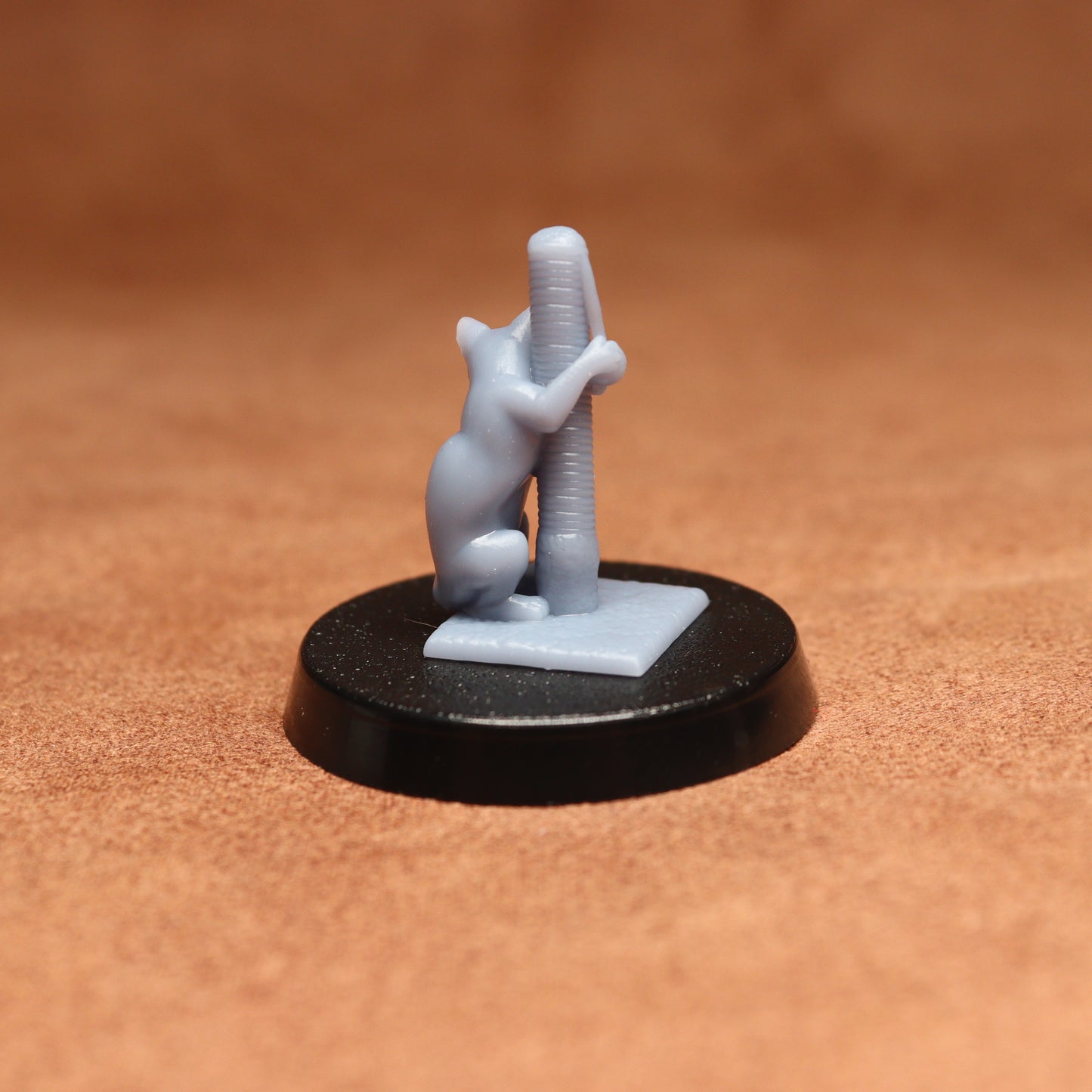 Small figurine of a cat climbing a pole on a black base against a brown background