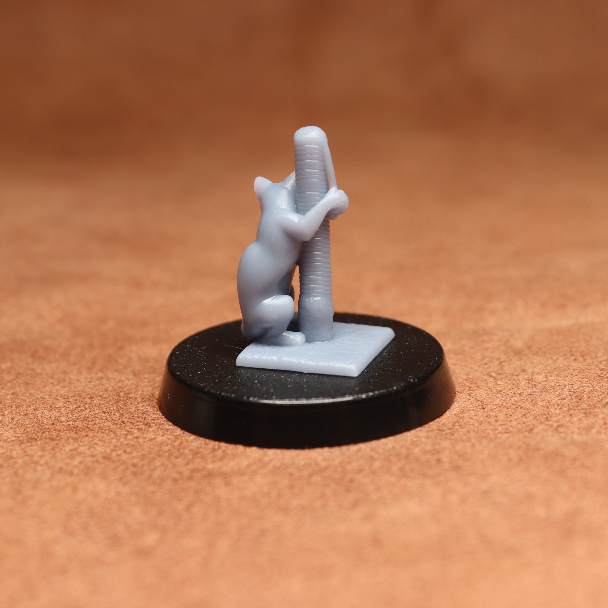 Small figurine of a cat climbing a pole on a black base against a brown background
