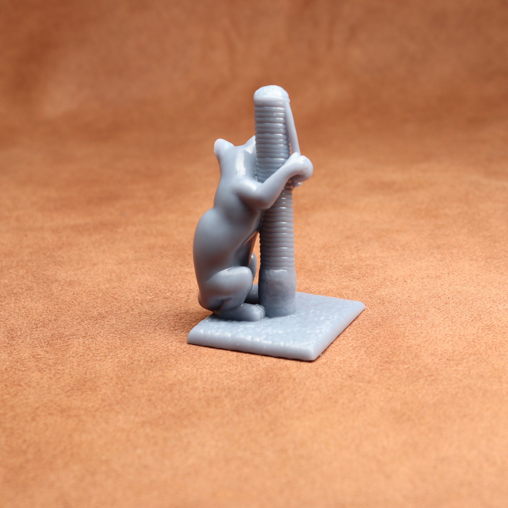 Gray 3D-printed figurine of a cat climbing a scratching post on an orange background