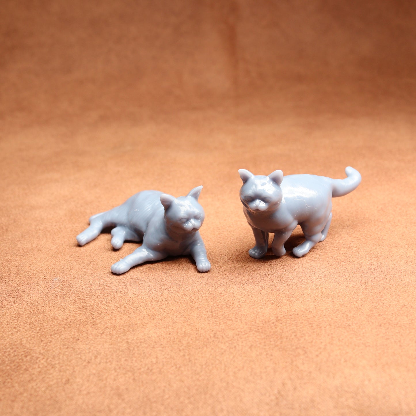 Two small gray cat figurines on a brown surface