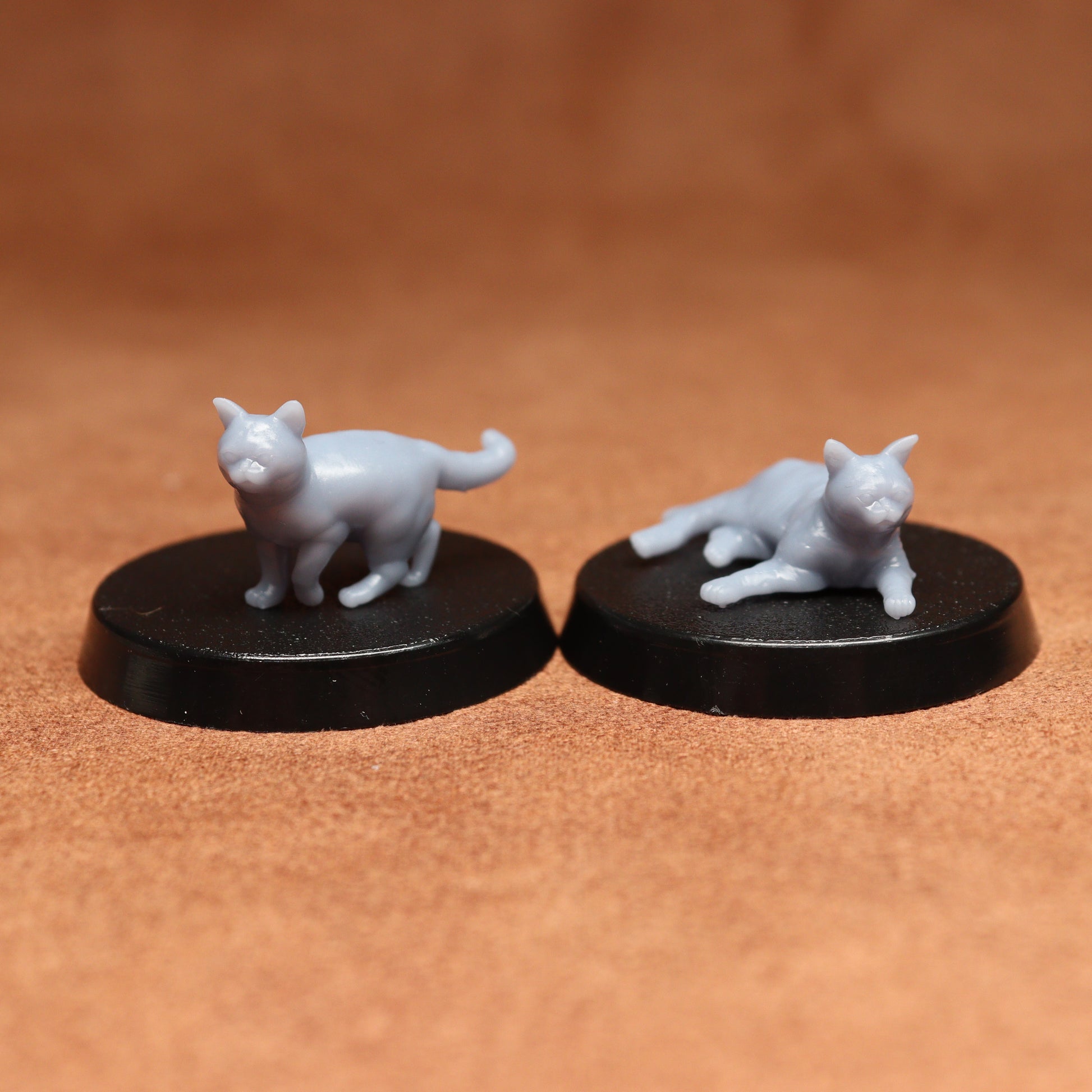 Two miniature cat figurines on black bases against a brown background