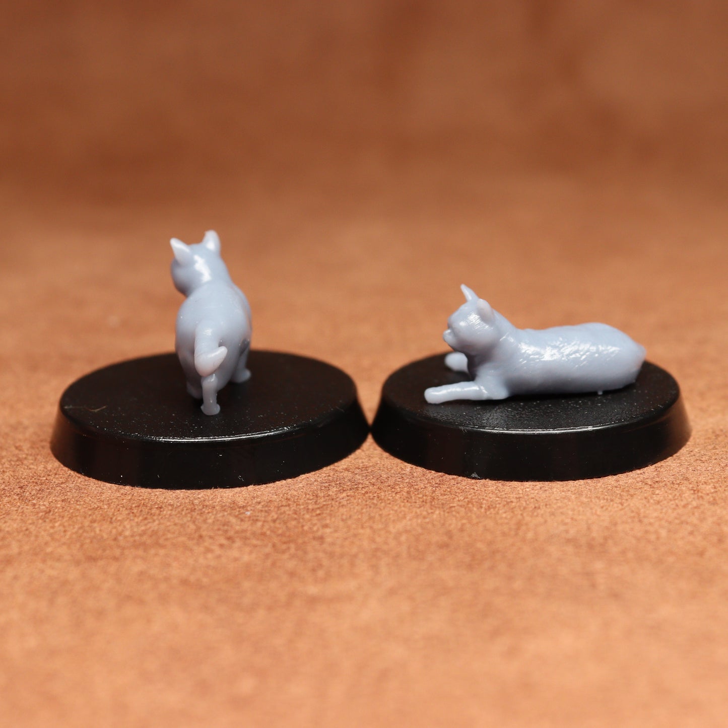 Two miniature cat figurines on black bases against a brown background