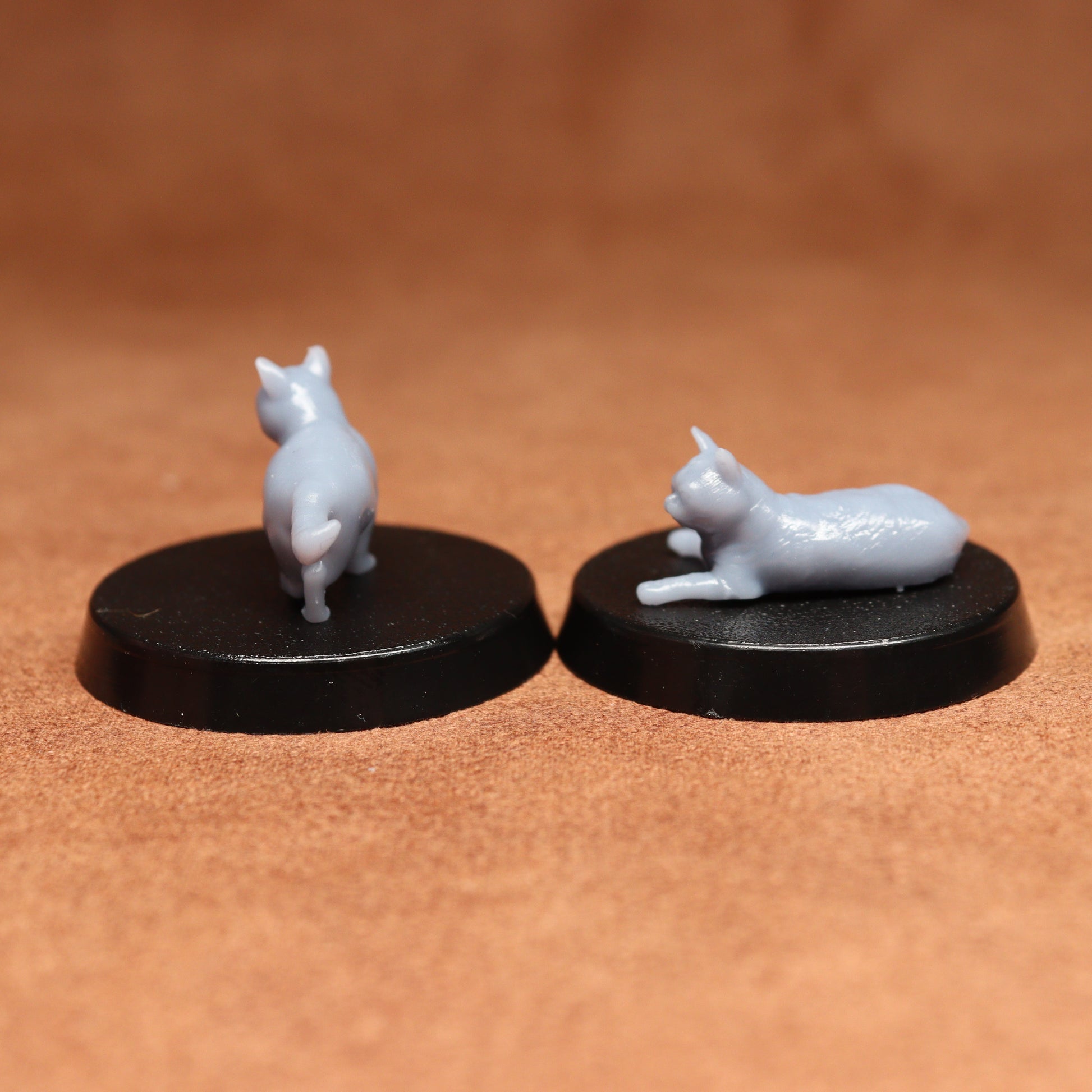 Two miniature cat figurines on black bases against a brown background
