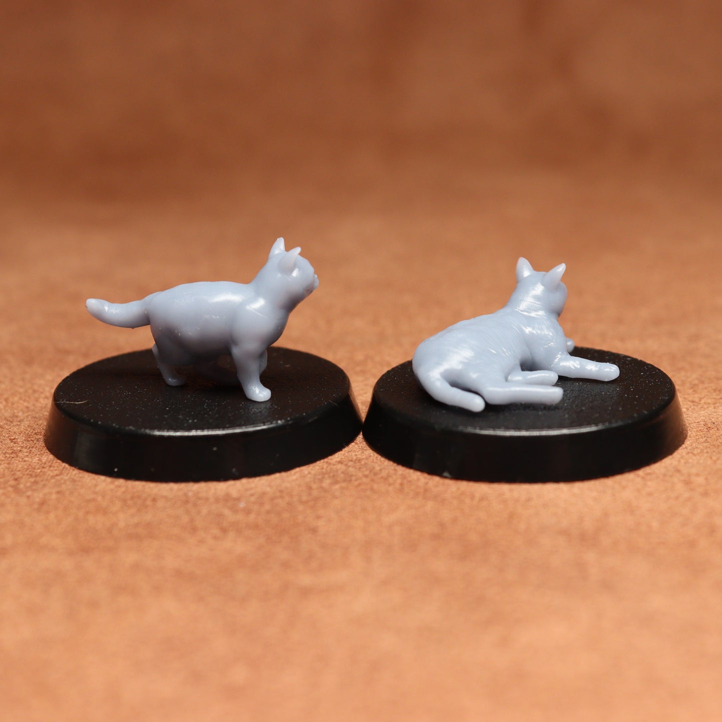 Two miniature cat figurines on black bases against a brown background