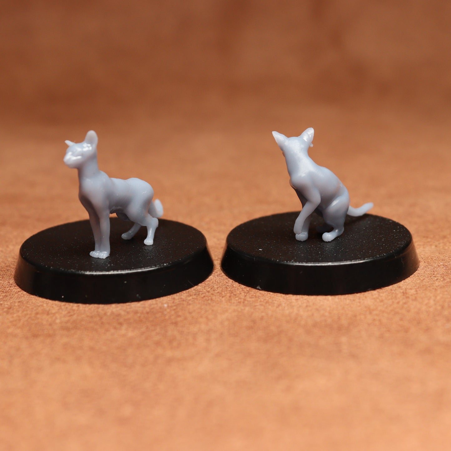 Two gray cat figurines on black bases against a brown background