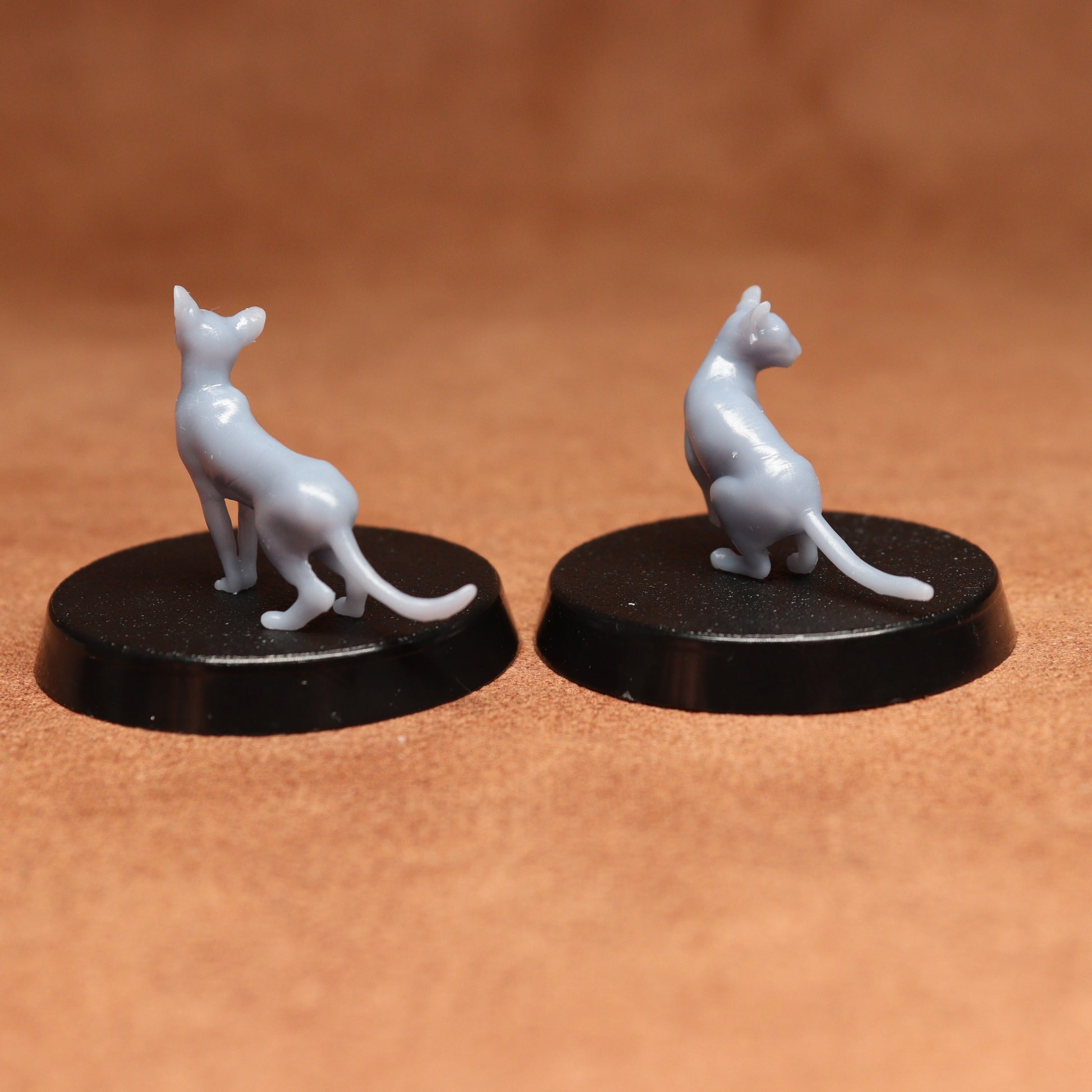 Two white cat figurines on black bases against a brown background