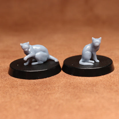 Two miniature cat figurines on black bases against a brown background