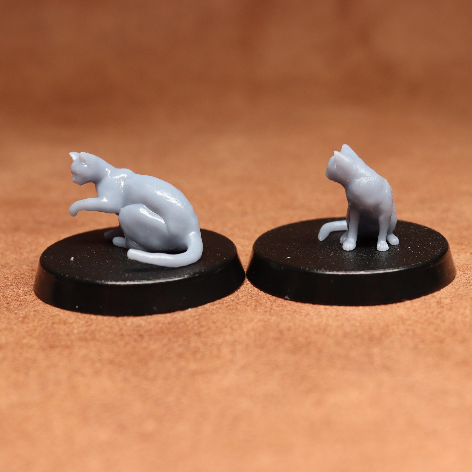 Two miniature cat figurines on black bases against a brown background