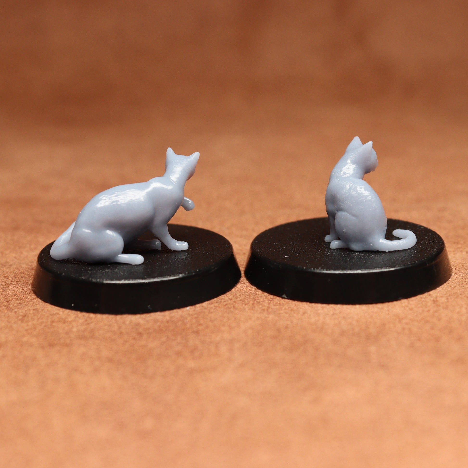 Two miniature cat figurines on black bases against a brown background