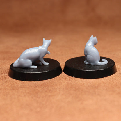 Two miniature cat figurines on black bases against a brown background