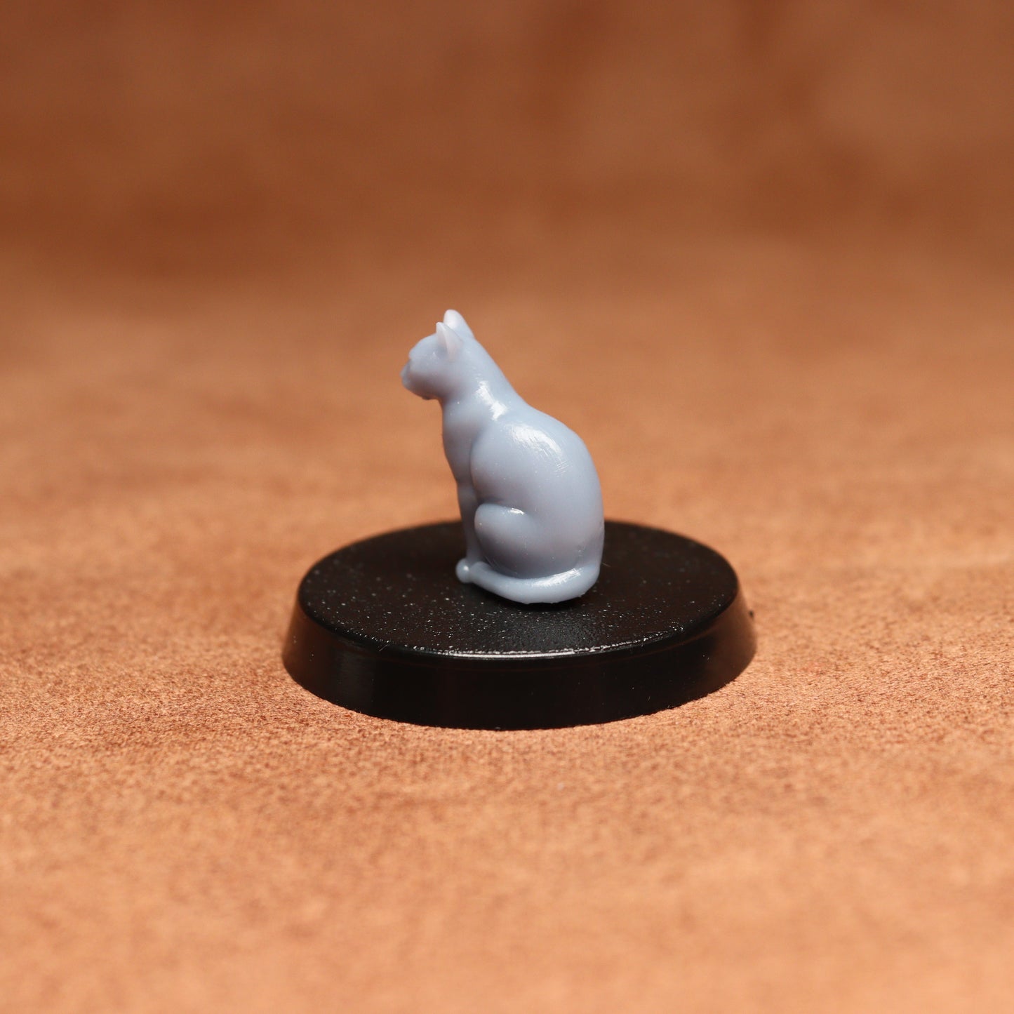 Small white cat figurine on a black round base against a brown background