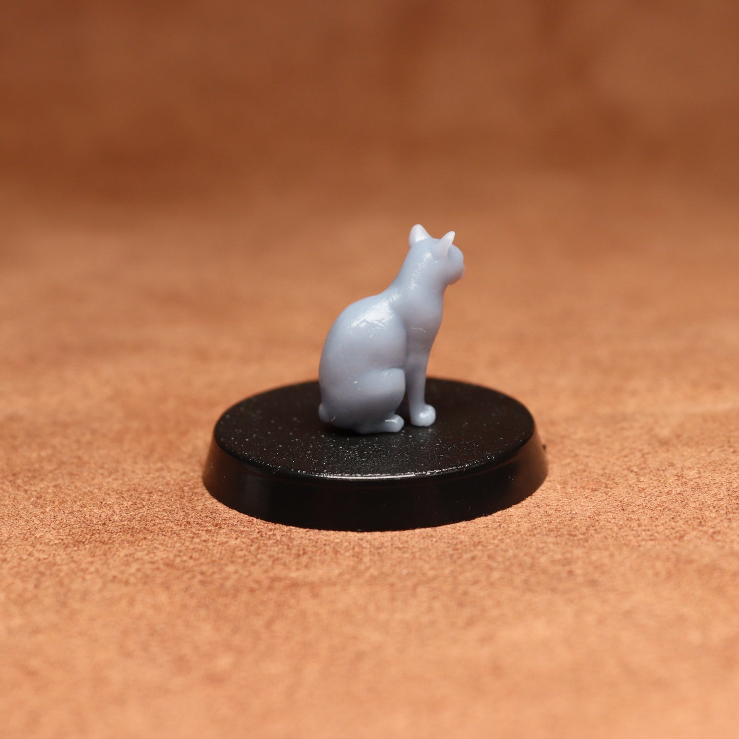 Small white cat figurine on a black round base against a brown background