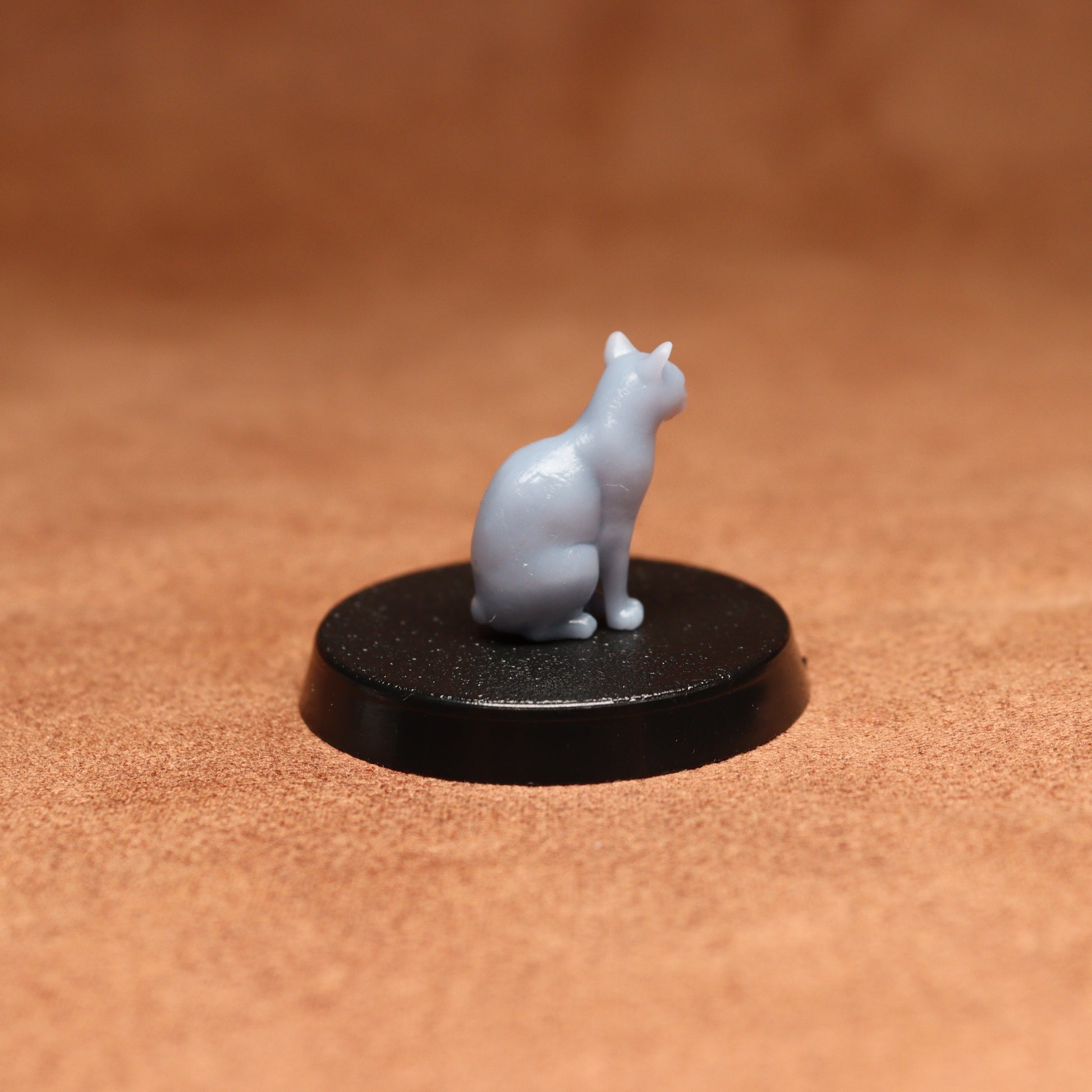 Small white cat figurine on a black round base against a brown background
