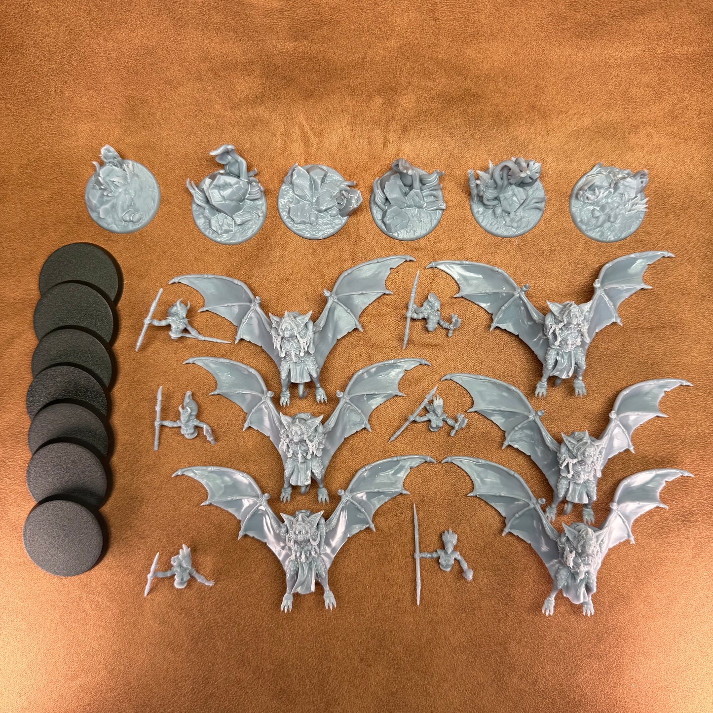 Collection of metallic bat figurines and round bases on a brown surface