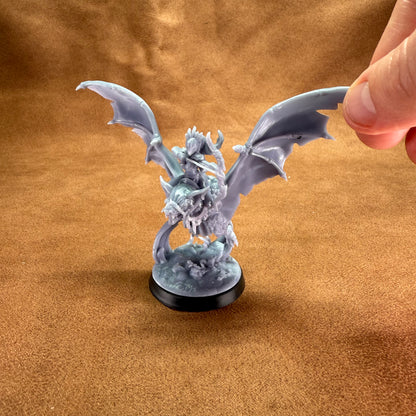 Miniature dragon figurine on a brown surface with a hand holding it by the tail.
