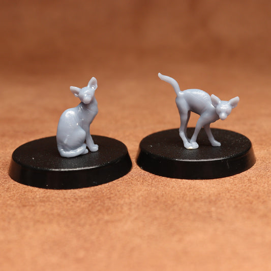 Two small cat figurines on black bases against a brown background