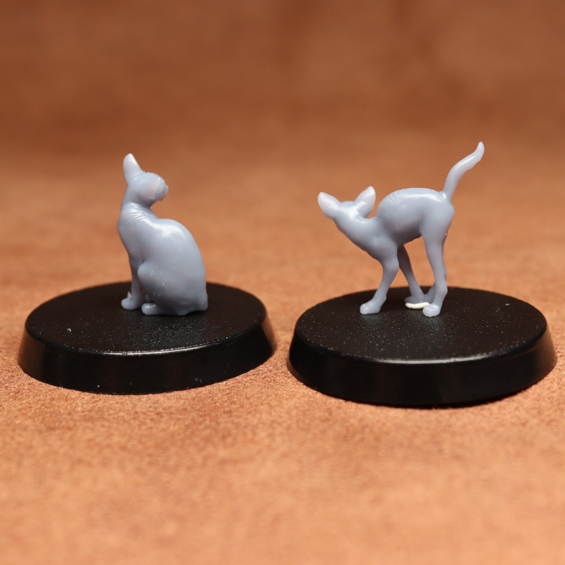 Two gray cat figurines on black bases against a brown background