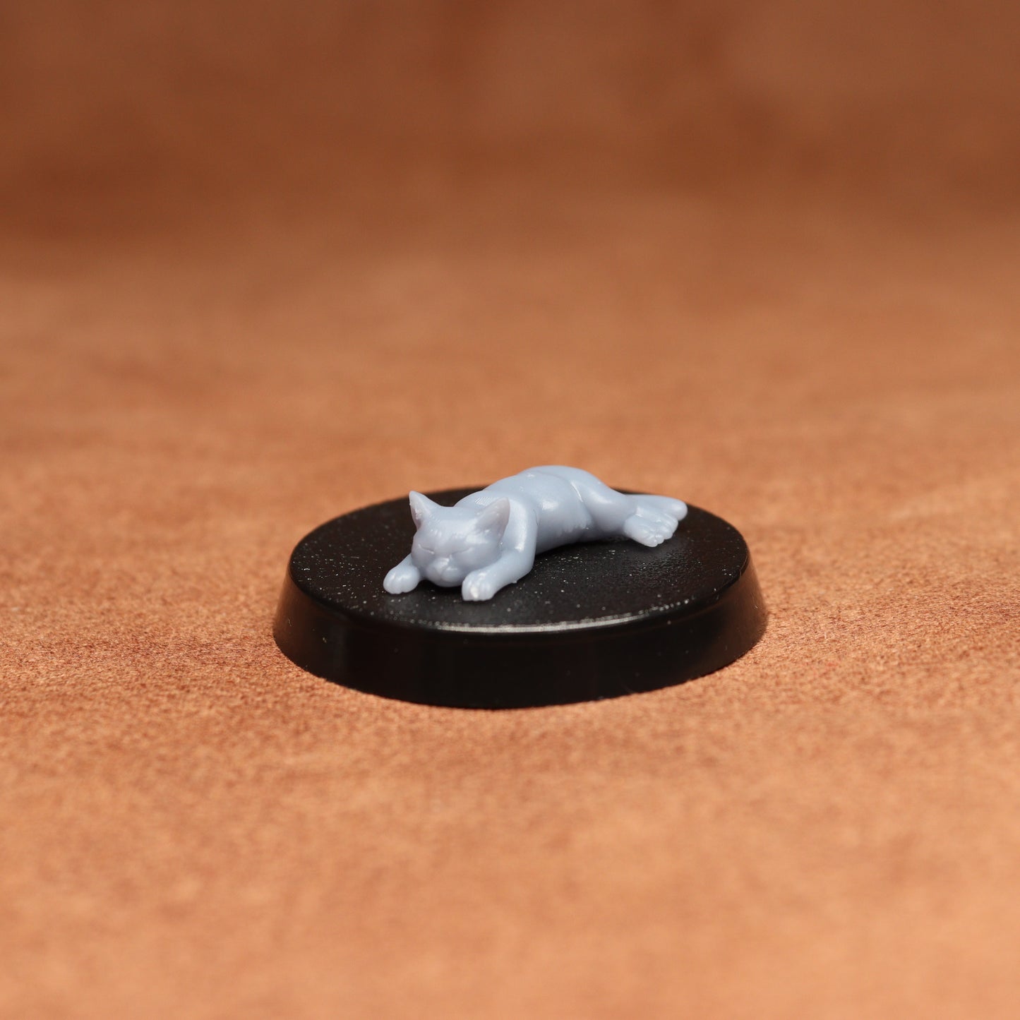Small figurine of a cat on a black round base against a brown background