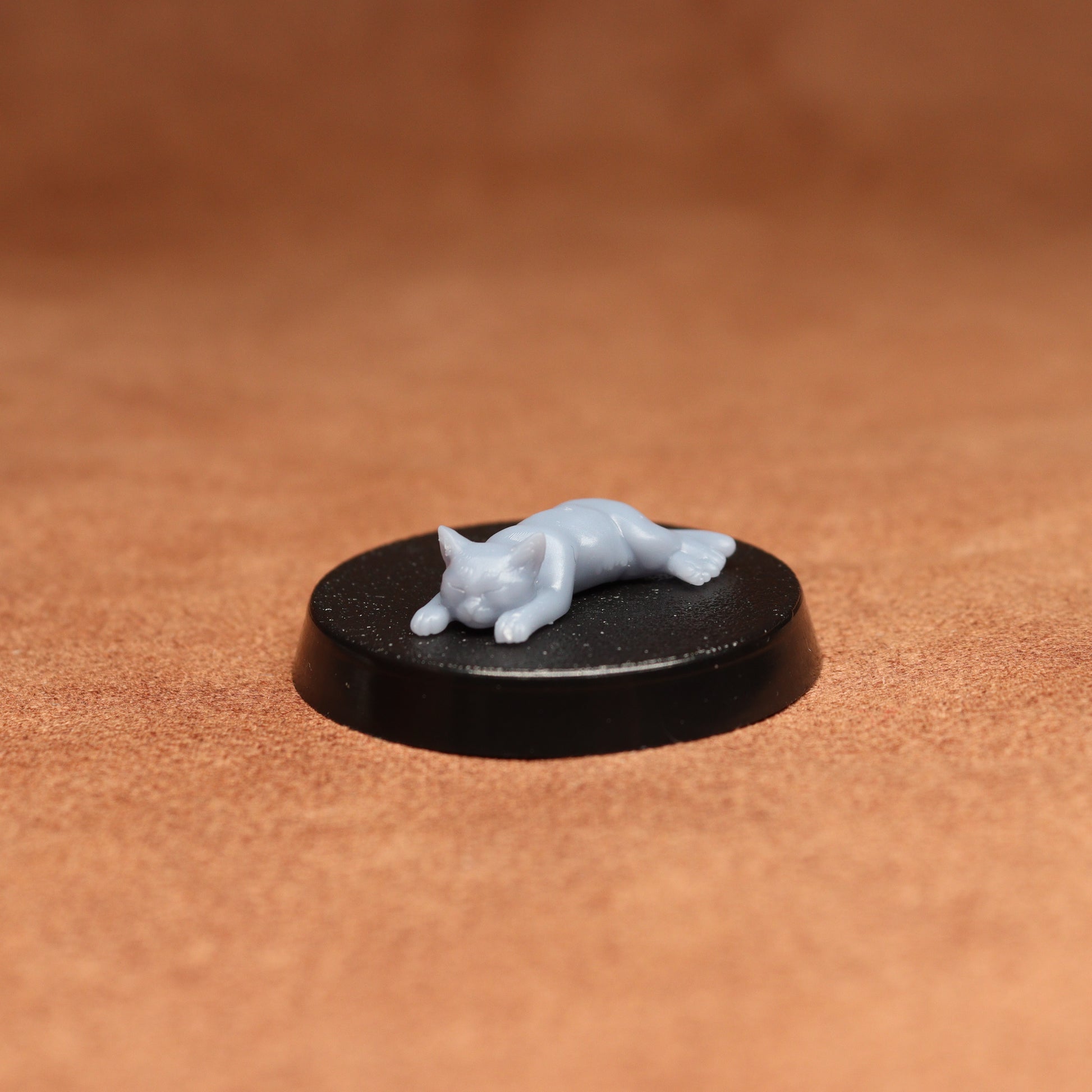 Small figurine of a cat on a black round base against a brown background