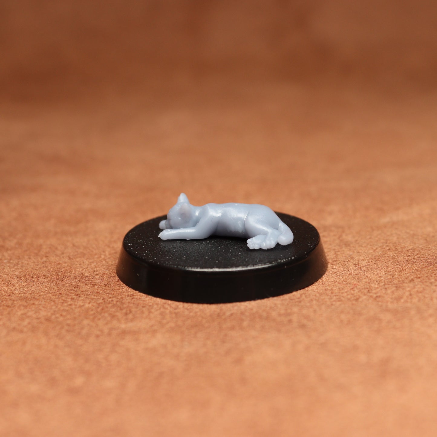 Small white figurine of a cat on a black round base against a brown background