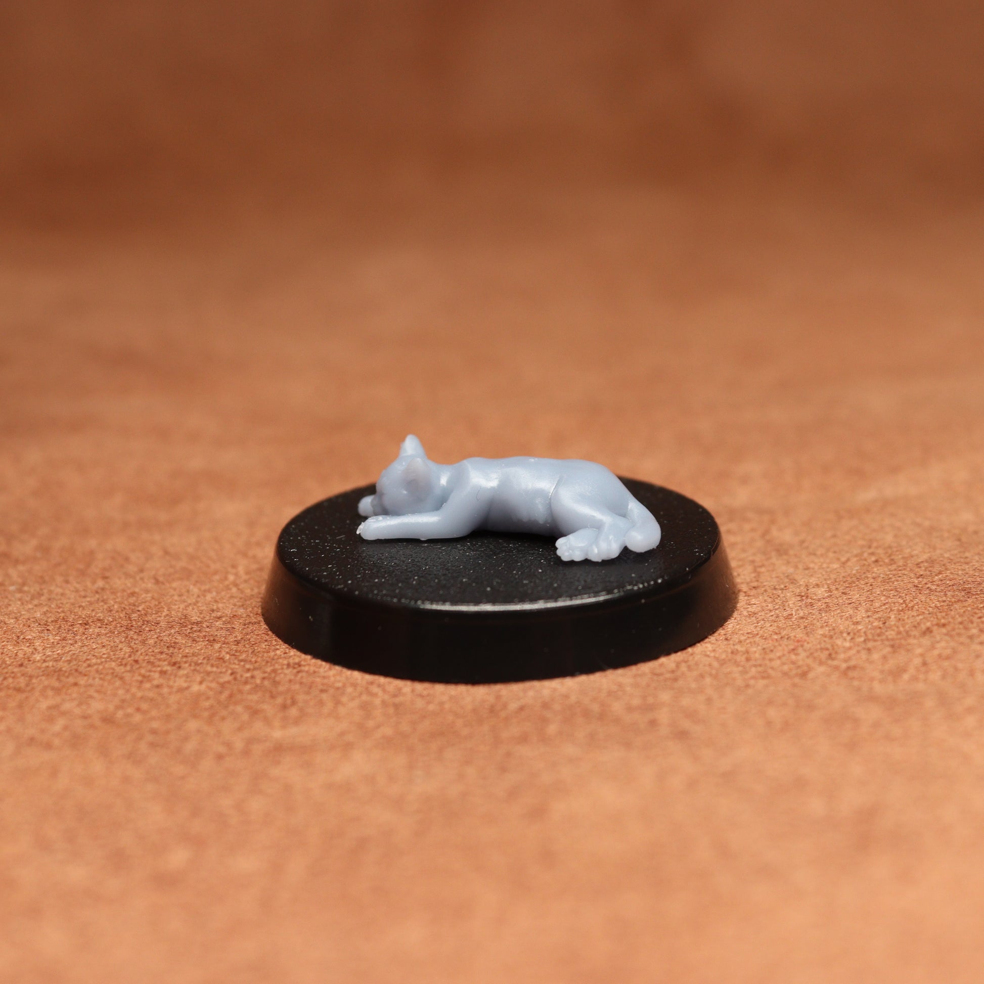 Small white figurine of a cat on a black round base against a brown background