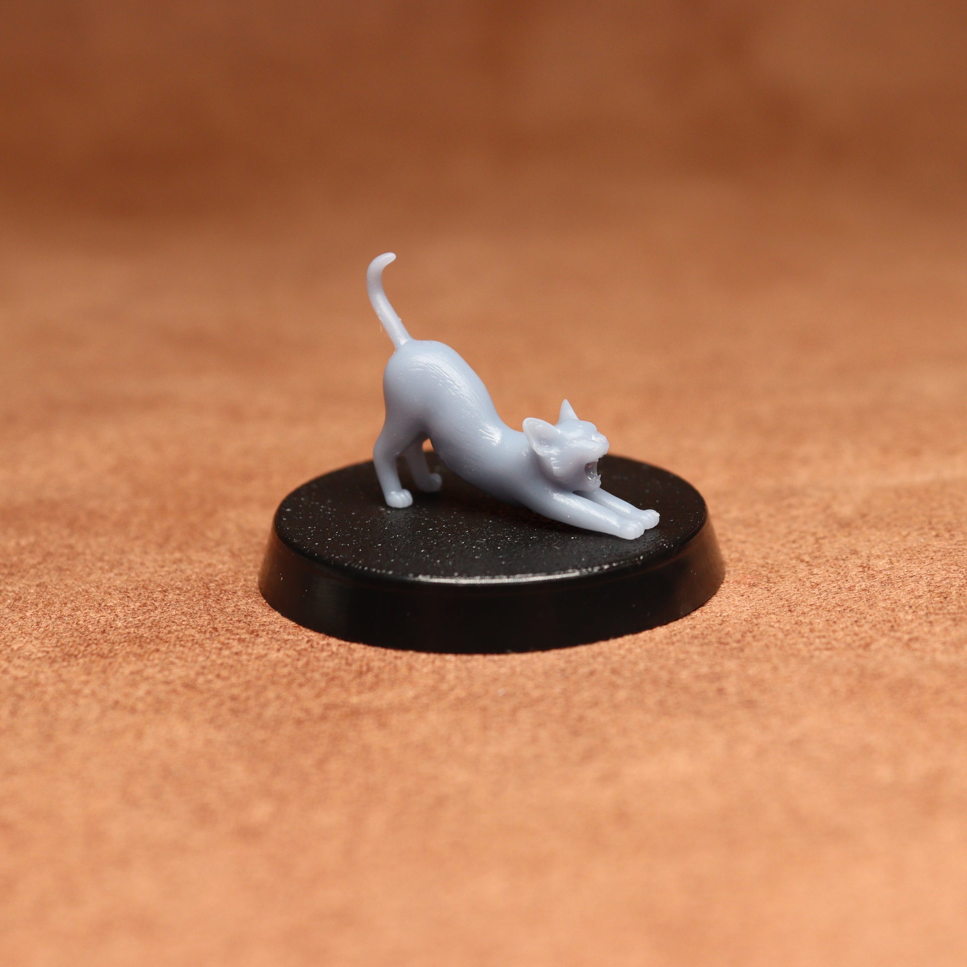 White cat figurine on a black round base against a brown background